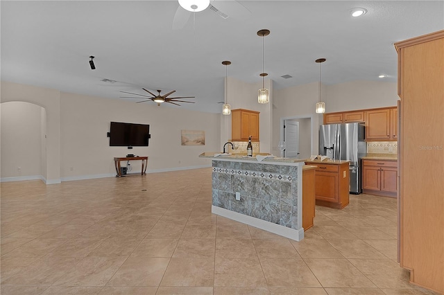 kitchen with tasteful backsplash, stainless steel fridge, an island with sink, decorative light fixtures, and light tile patterned floors