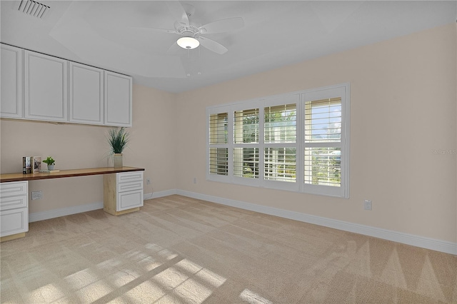 unfurnished office with a raised ceiling, ceiling fan, light colored carpet, and built in desk