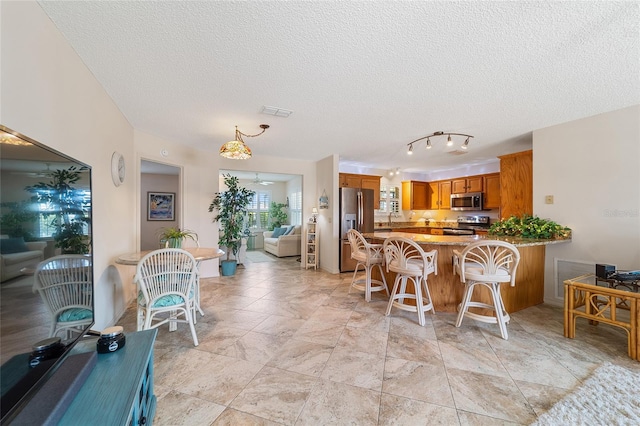 interior space with a textured ceiling, a kitchen bar, kitchen peninsula, and stainless steel appliances