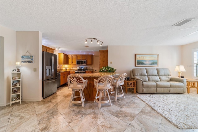 kitchen with kitchen peninsula, a textured ceiling, a breakfast bar, and stainless steel appliances