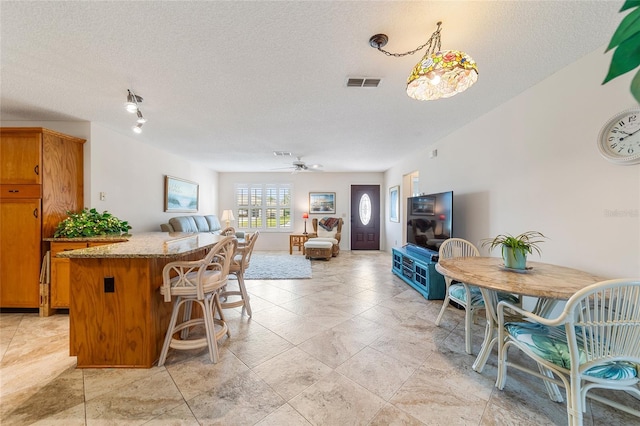 kitchen featuring pendant lighting, ceiling fan, light stone counters, and a textured ceiling