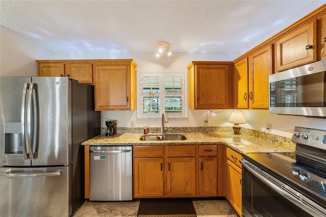 kitchen with a textured ceiling, light stone counters, sink, and stainless steel appliances