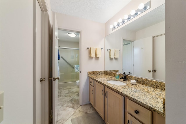 bathroom with vanity, toilet, a shower with door, and a textured ceiling