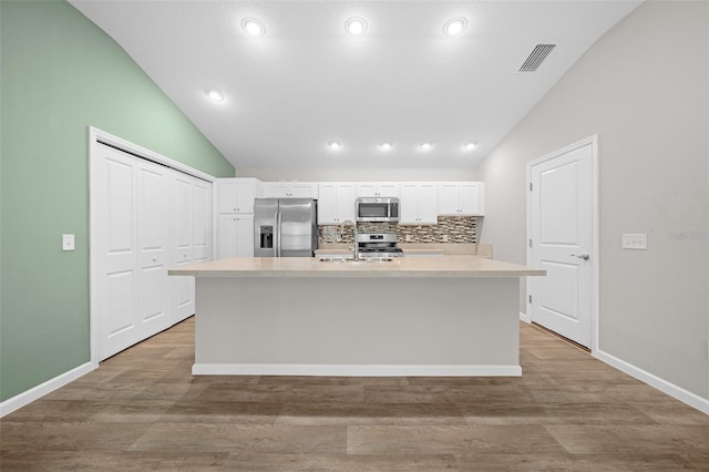 kitchen with white cabinets, appliances with stainless steel finishes, a center island with sink, and lofted ceiling