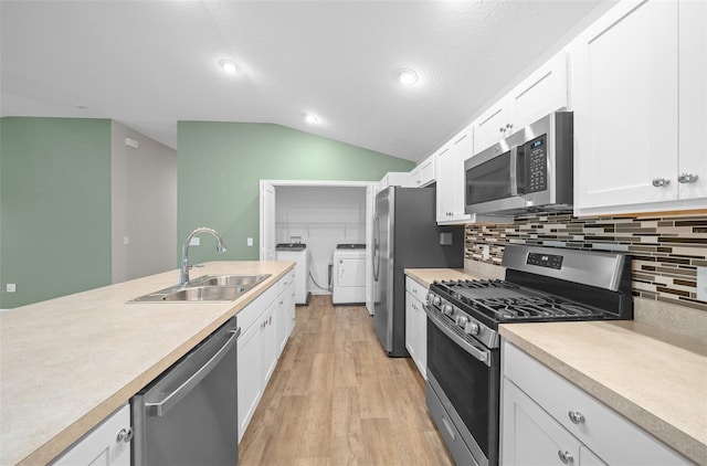 kitchen with washing machine and clothes dryer, sink, stainless steel appliances, vaulted ceiling, and white cabinets