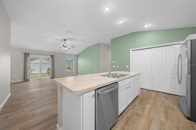 kitchen with appliances with stainless steel finishes, a kitchen island with sink, sink, white cabinetry, and lofted ceiling