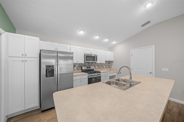 kitchen with appliances with stainless steel finishes, vaulted ceiling, a kitchen island with sink, sink, and white cabinetry