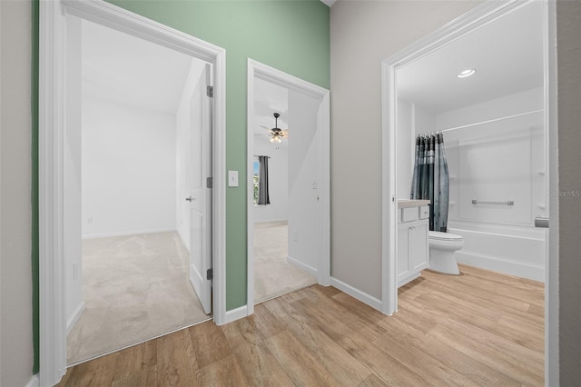 interior space featuring vanity, ceiling fan, shower / bathtub combination with curtain, hardwood / wood-style floors, and toilet