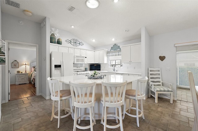 kitchen with white cabinetry, a kitchen island, white appliances, and a breakfast bar area