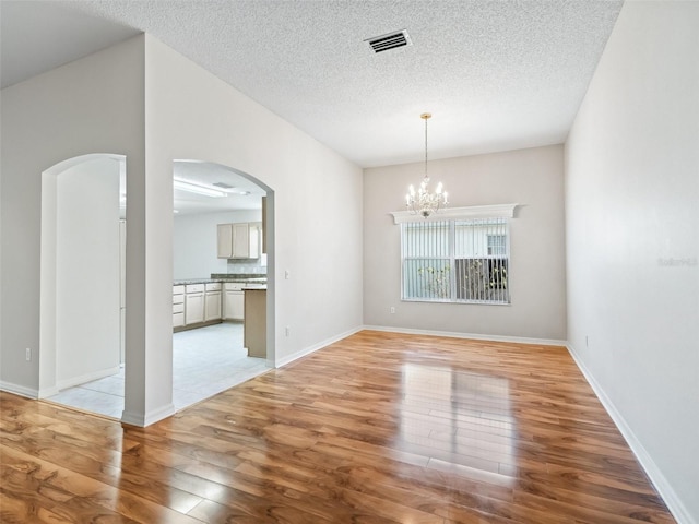 unfurnished dining area with an inviting chandelier, a textured ceiling, and light hardwood / wood-style flooring