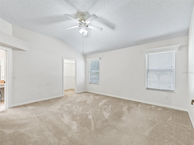 unfurnished bedroom with multiple windows, a spacious closet, ceiling fan, and lofted ceiling