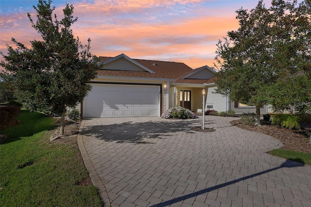 ranch-style house with an attached garage, decorative driveway, and a front yard