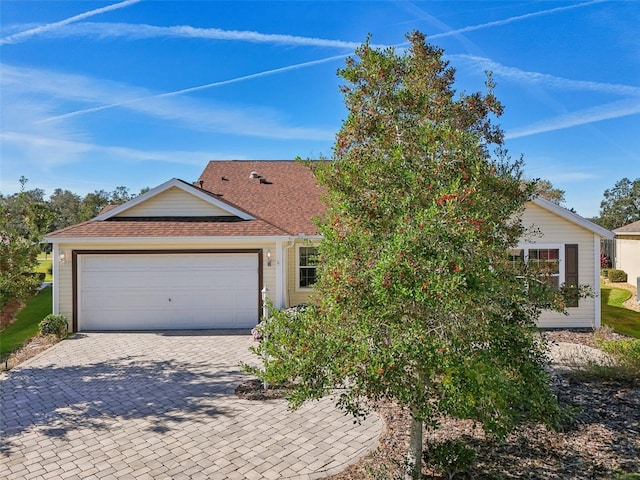 ranch-style home with a garage, a shingled roof, and decorative driveway