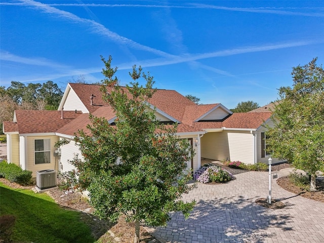 view of front of house with a shingled roof, decorative driveway, and central air condition unit