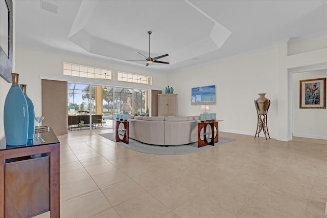 tiled living room with ceiling fan and a tray ceiling