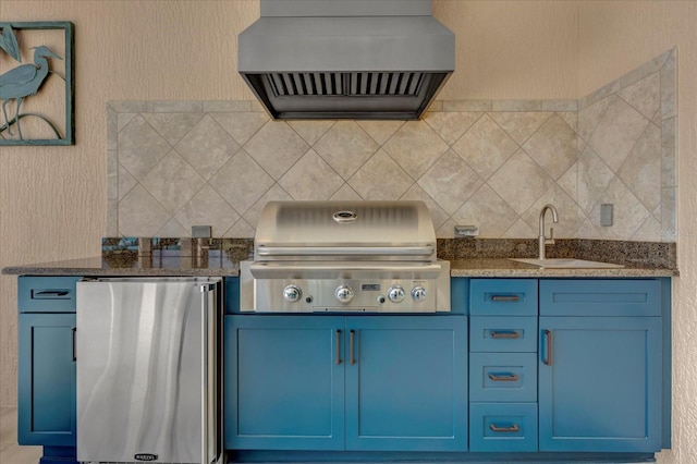 kitchen with blue cabinetry, refrigerator, custom range hood, and sink