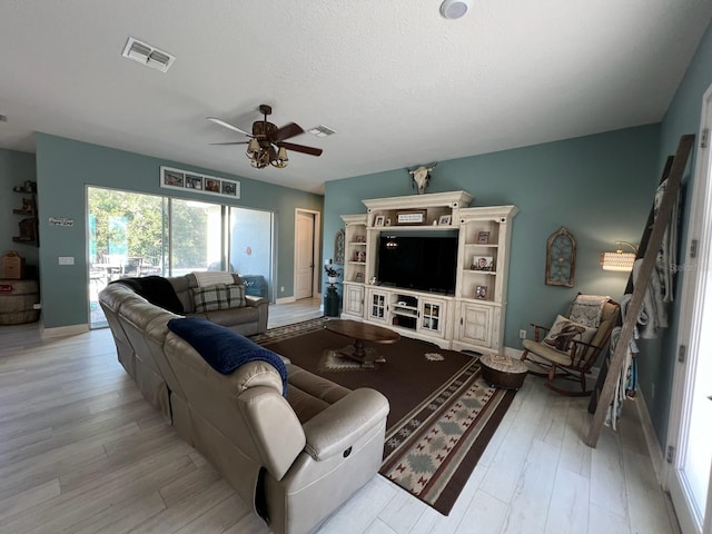 living room with ceiling fan, light wood-type flooring, and a textured ceiling