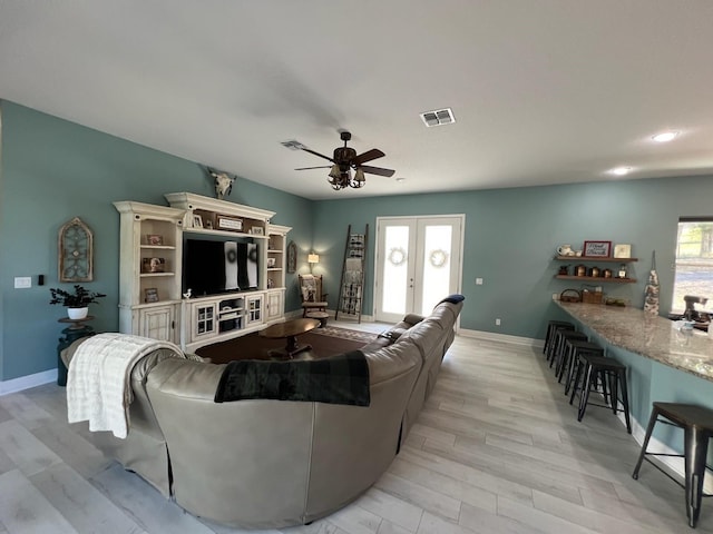 living room featuring a wealth of natural light, french doors, ceiling fan, and light hardwood / wood-style flooring