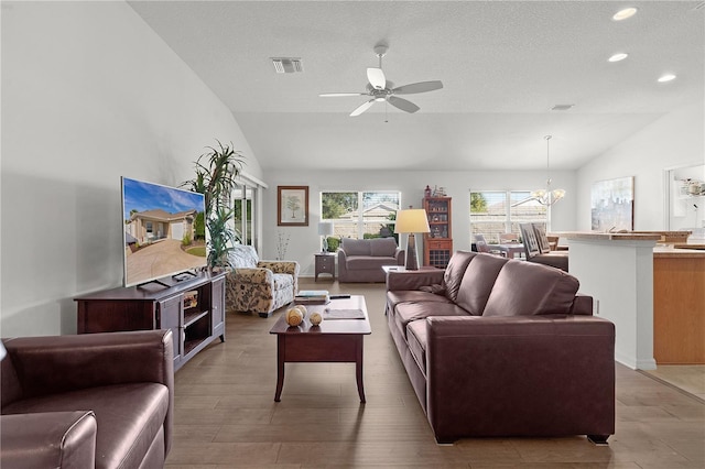 living room featuring a textured ceiling, ceiling fan with notable chandelier, hardwood / wood-style flooring, and vaulted ceiling