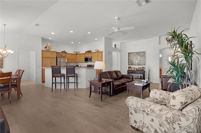 living room featuring ceiling fan with notable chandelier, light hardwood / wood-style floors, and a towering ceiling