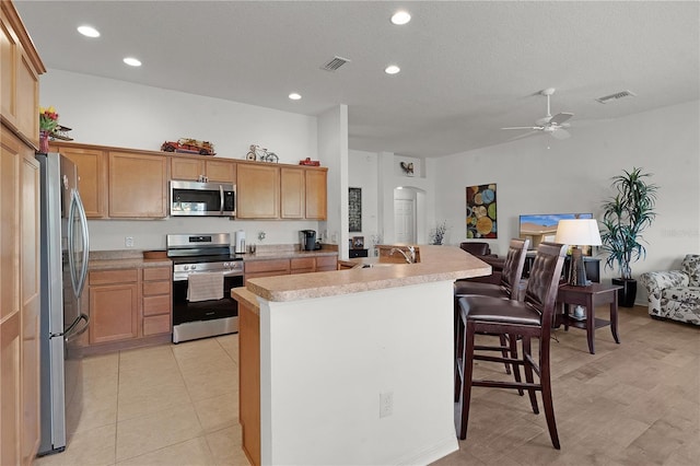 kitchen with a kitchen island with sink, sink, a breakfast bar area, ceiling fan, and stainless steel appliances