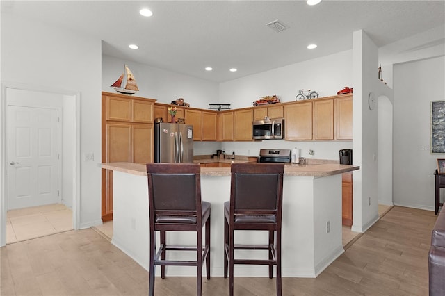 kitchen with a breakfast bar area, a kitchen island with sink, stainless steel appliances, and light hardwood / wood-style floors