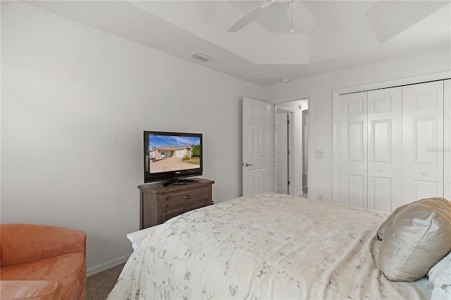 carpeted bedroom featuring a tray ceiling, a closet, and ceiling fan