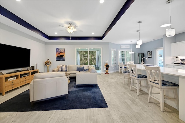 living room with ceiling fan, light hardwood / wood-style floors, sink, and a tray ceiling