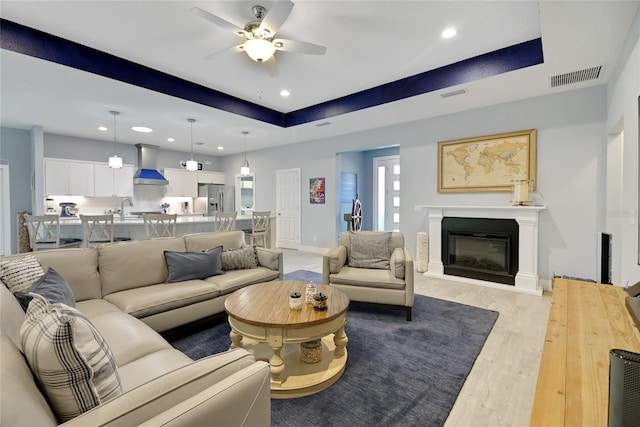 living room with ceiling fan, light hardwood / wood-style floors, a raised ceiling, and sink