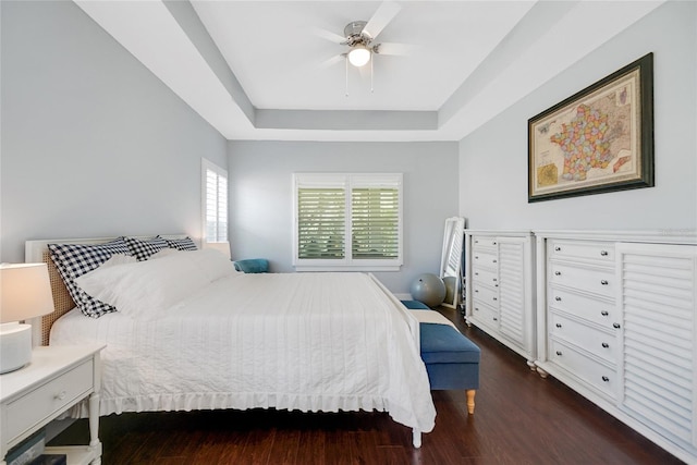 bedroom with a tray ceiling, ceiling fan, and dark wood-type flooring