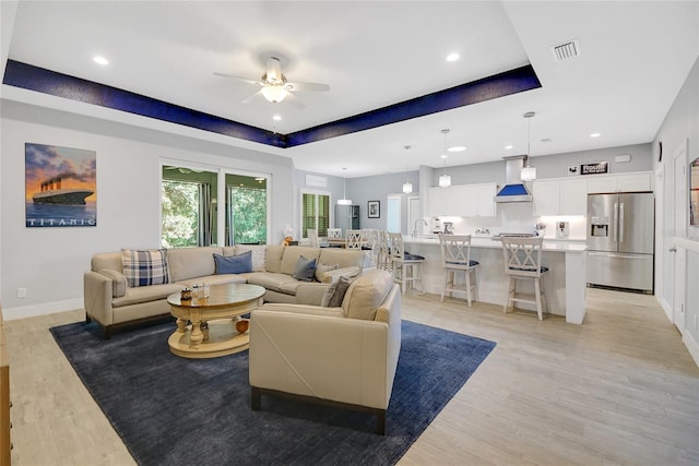 living room with ceiling fan, a raised ceiling, sink, and light hardwood / wood-style flooring