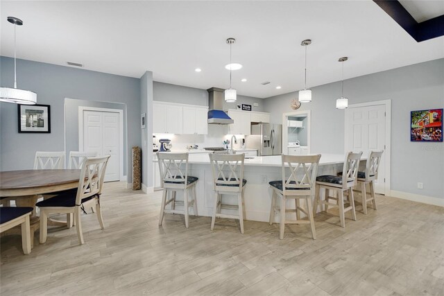 kitchen with a large island, pendant lighting, stainless steel fridge with ice dispenser, white cabinetry, and a breakfast bar area