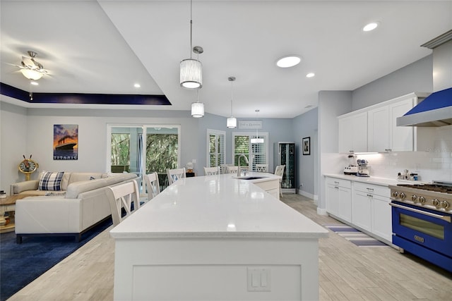 kitchen with a center island with sink, white cabinets, pendant lighting, and high end stainless steel range oven