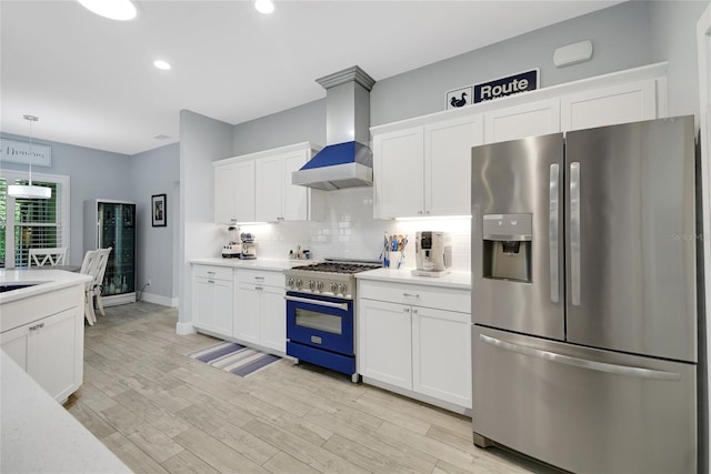 kitchen featuring appliances with stainless steel finishes, light wood-type flooring, wall chimney exhaust hood, pendant lighting, and white cabinets