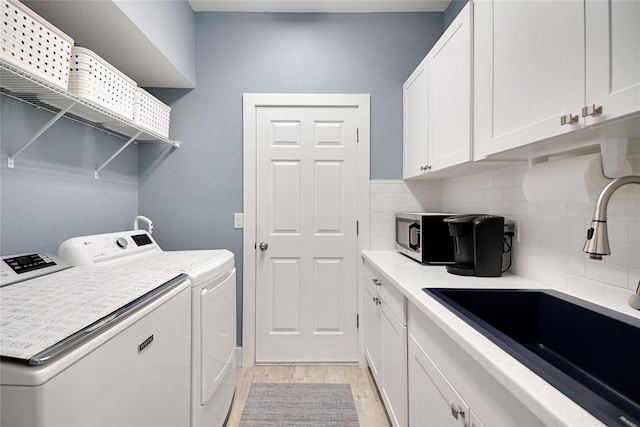 laundry room with washer and clothes dryer, cabinets, sink, and light hardwood / wood-style flooring