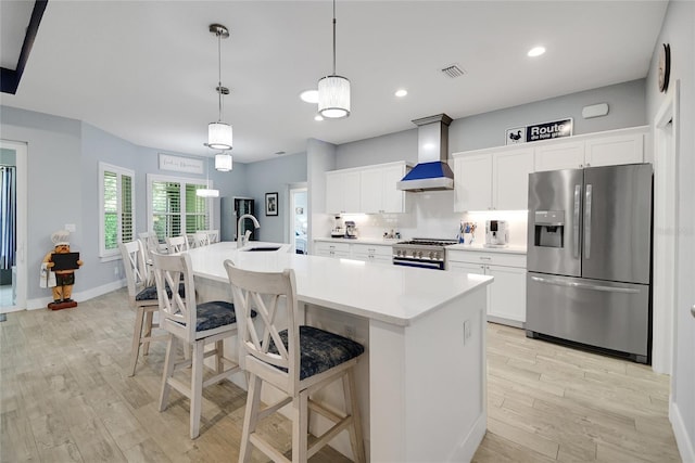 kitchen featuring pendant lighting, stainless steel appliances, a kitchen island with sink, and wall chimney exhaust hood