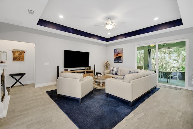 living room featuring ceiling fan, wood-type flooring, and a tray ceiling