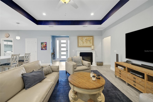 living room featuring wood-type flooring, a raised ceiling, and ceiling fan