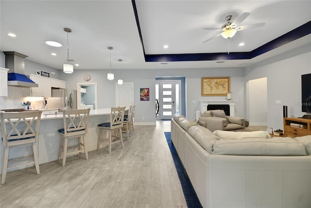 living room featuring light wood-type flooring, a raised ceiling, and ceiling fan