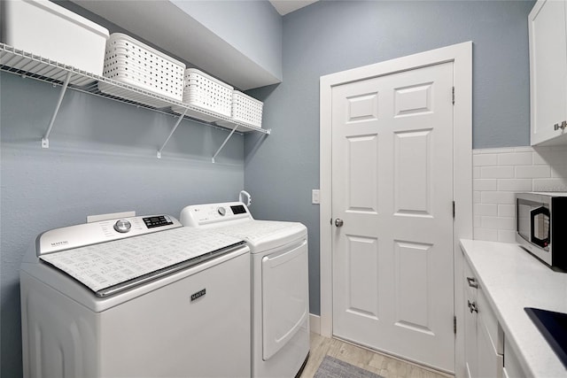 clothes washing area with washer and clothes dryer, cabinets, and light hardwood / wood-style flooring