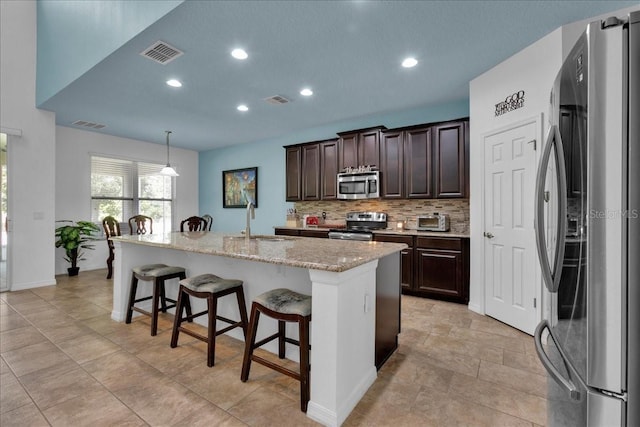 kitchen with sink, stainless steel appliances, a kitchen breakfast bar, an island with sink, and pendant lighting