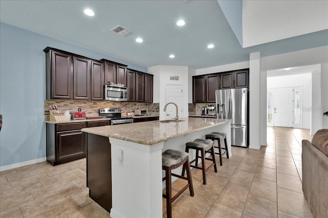 kitchen with light stone countertops, sink, an island with sink, a breakfast bar, and appliances with stainless steel finishes