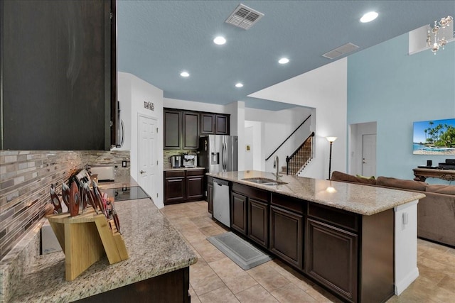 kitchen featuring sink, light stone counters, backsplash, an island with sink, and appliances with stainless steel finishes