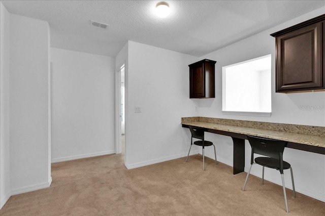 unfurnished office featuring a textured ceiling, built in desk, and light carpet