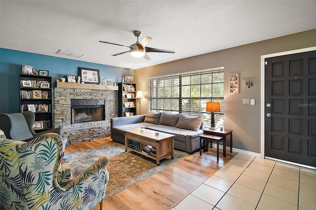 living room featuring ceiling fan, light tile patterned flooring, a stone fireplace, and a textured ceiling