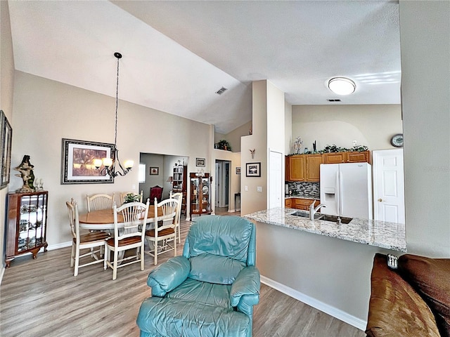 kitchen featuring light hardwood / wood-style flooring, decorative backsplash, light stone countertops, white fridge with ice dispenser, and decorative light fixtures