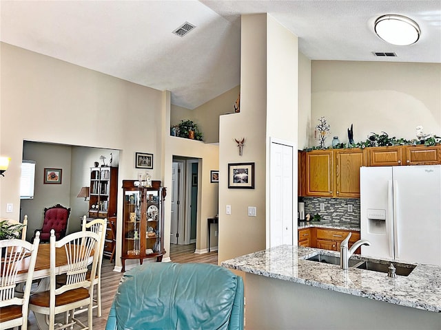 kitchen featuring sink, light stone counters, white refrigerator with ice dispenser, backsplash, and light wood-type flooring