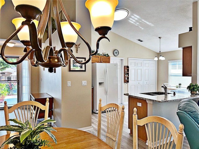 kitchen with light stone counters, sink, white refrigerator with ice dispenser, a chandelier, and lofted ceiling