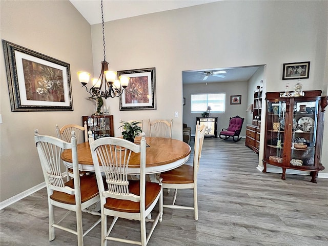 dining room featuring ceiling fan with notable chandelier, wood-type flooring, and high vaulted ceiling