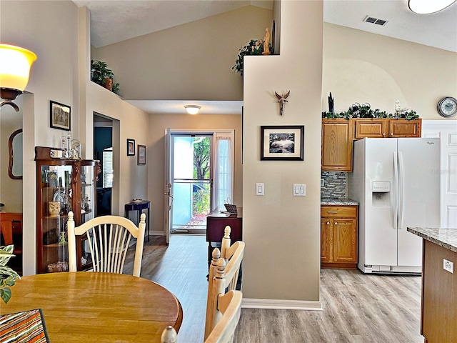 dining space featuring high vaulted ceiling and light hardwood / wood-style flooring